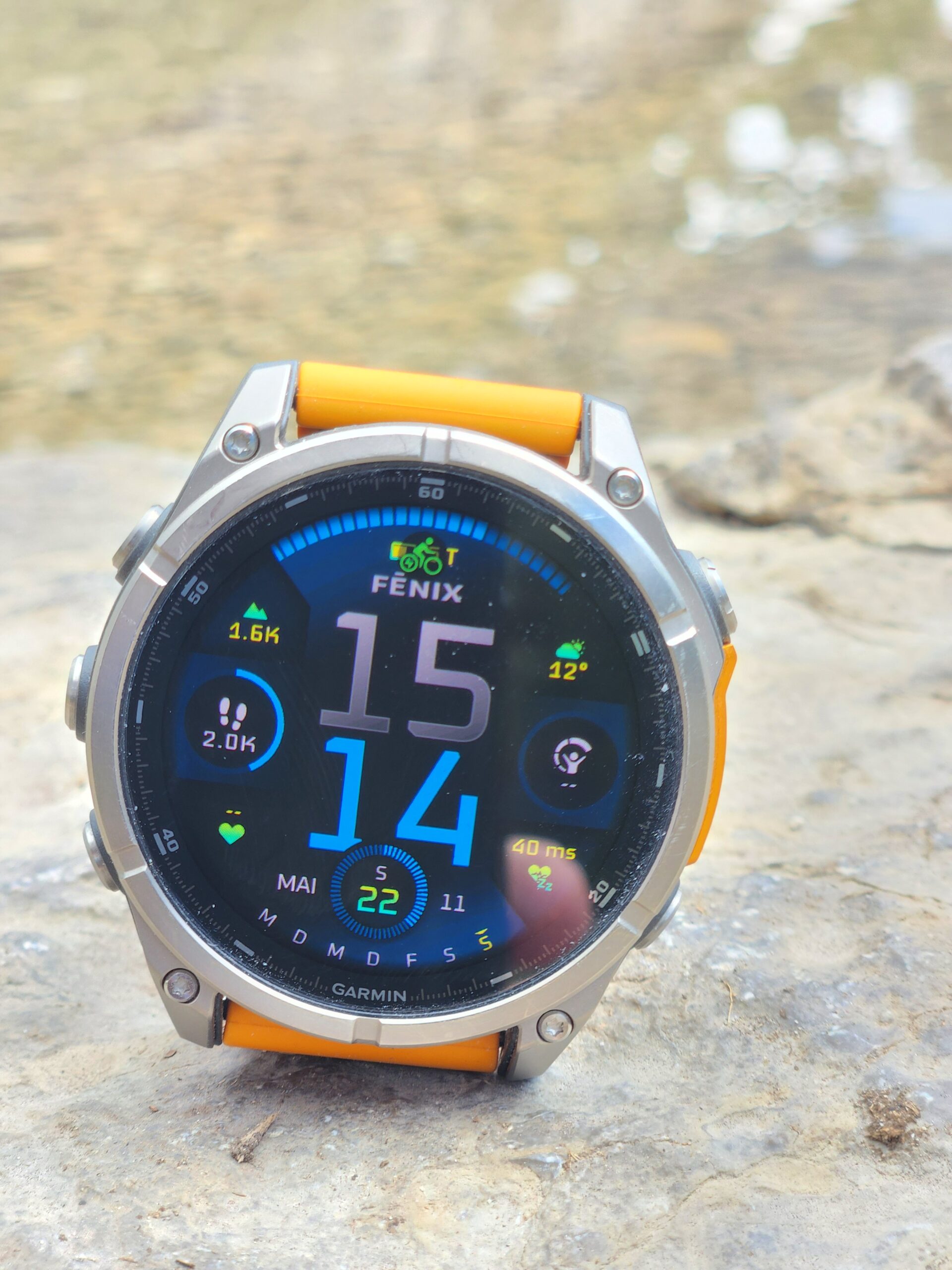 Garmin Fenix 8 auf einem Stein, Display mit Uhrzeit, Schritten und Puls